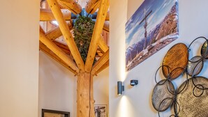 Een houten plafondconstructie met een decoratieve plantenarrangement, een ingelijste foto aan de muur en een wandlamp.