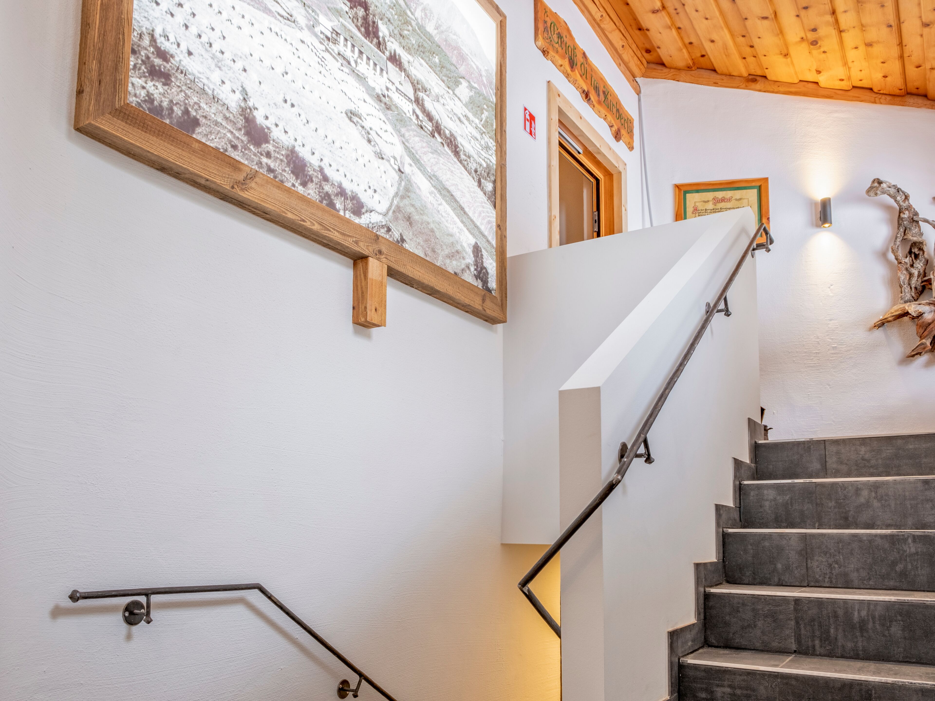 Un escalier avec une rampe métallique, un cadre en bois contenant une image et un luminaire fixé au mur.