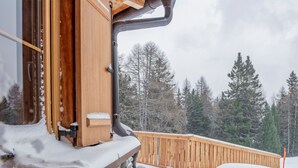 Een houten terras met sneeuw, een stenen muur en uitzicht op een bebost gebied.