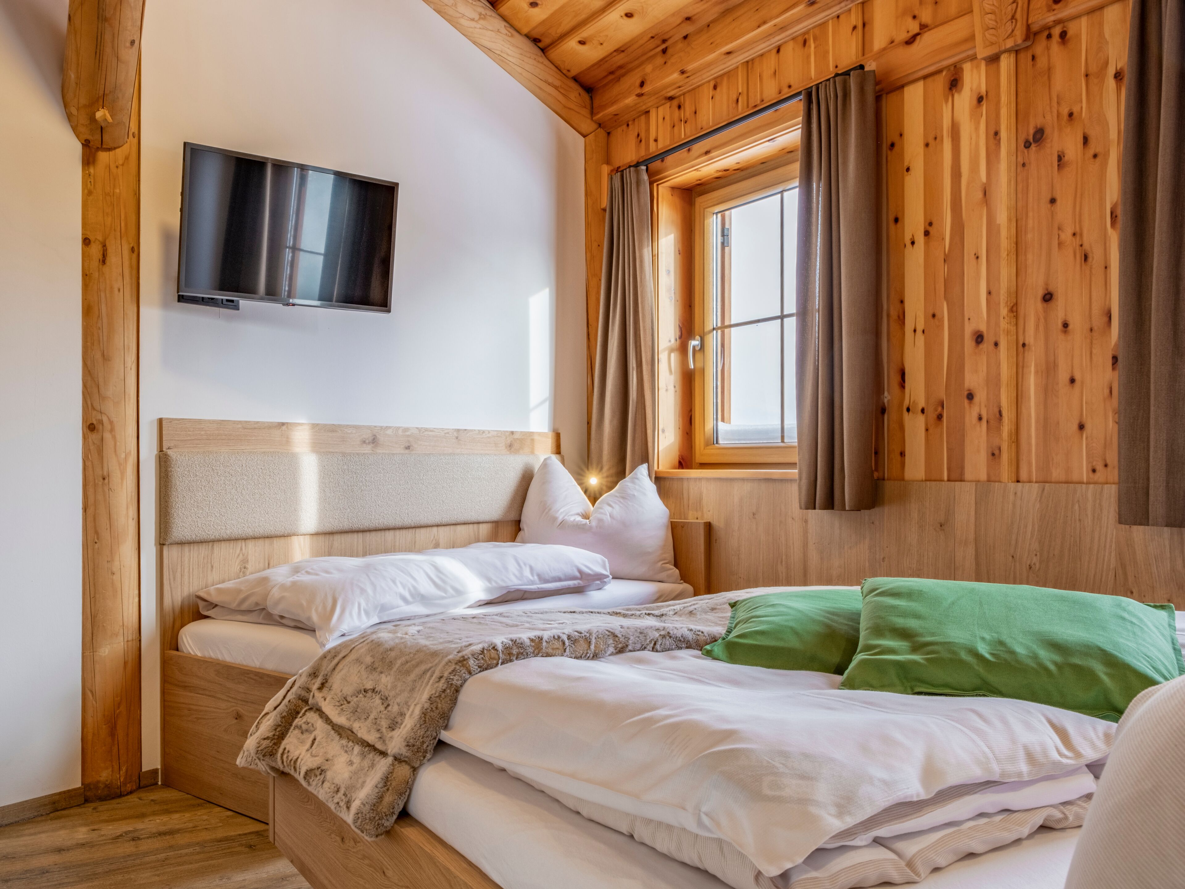 Een houten kamer met een bed, een tv aan de muur en een raam met gordijnen.