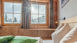 A cozy bedroom with a wooden headboard, a window with curtains, and a view of a snowy forest. - Luxurious apartment with a sauna on the slope (Weißpriach)