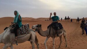 Paisagem desértica com camelos e pessoas a cavalo.