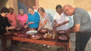 Um grupo de pessoas ao redor de uma mesa com diversos pratos e uma garrafa, possivelmente preparando ou servindo comida.