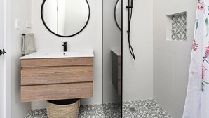 Ein modernes Badezimmer mit einem Holzwaschtisch, einem runden Spiegel und einer Dusche mit schwarzem Brauseschlauch.