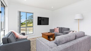 Ein modernes Wohnzimmer mit grauen Sofas, einem Flachbildfernseher, einer Stehlampe und einem kleinen Holztisch.