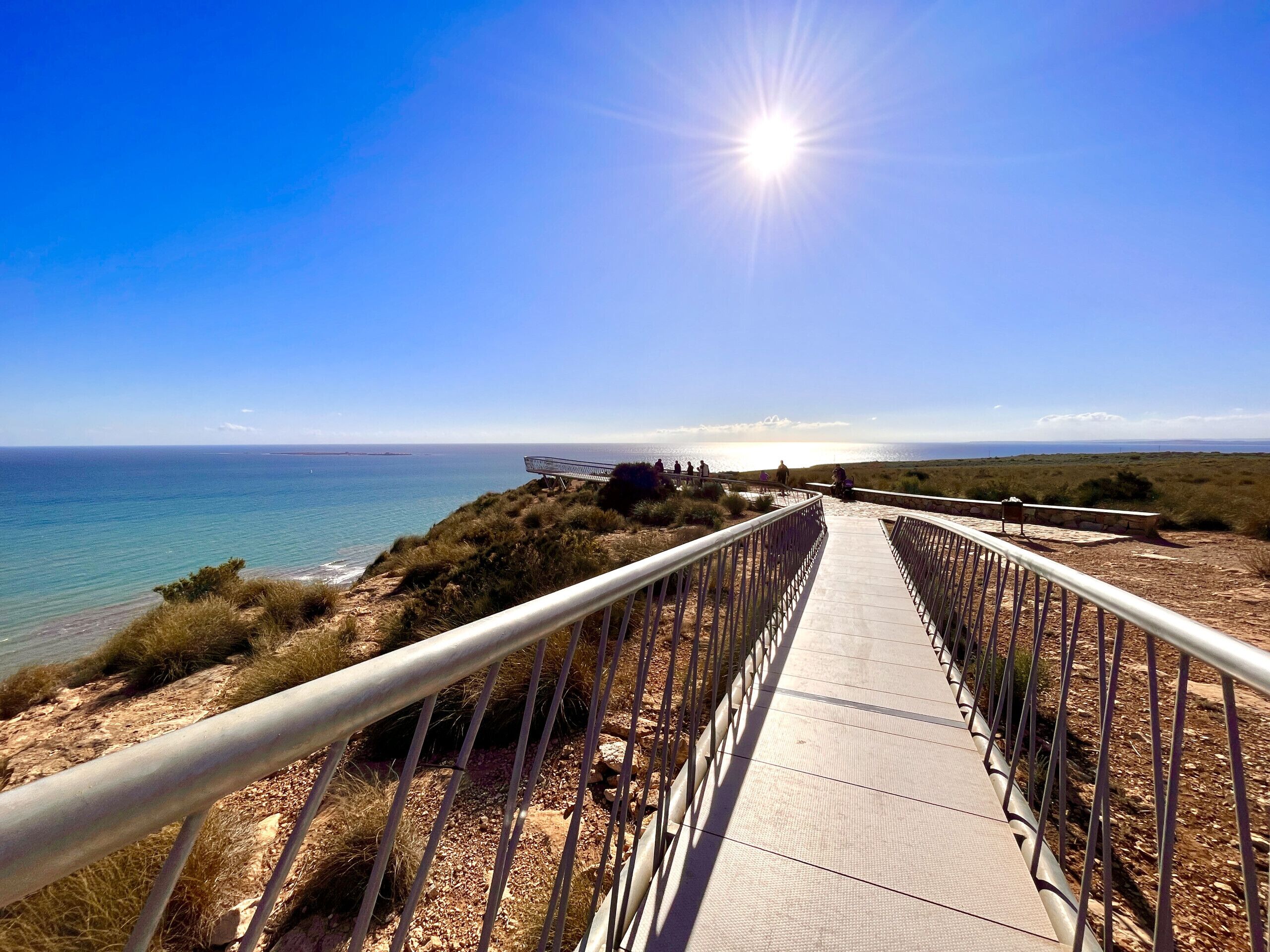 A wooden boardwalk leading to a beach with a metal railing, overlooking the ocean.
