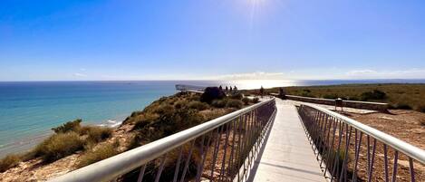 A wooden boardwalk leading to a beach with a metal railing, overlooking the ocean.