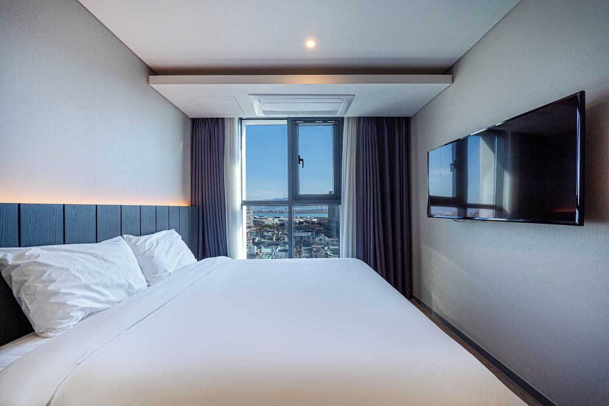A hotel room with a large bed, a flat-screen TV mounted on the wall, and a window with curtains.