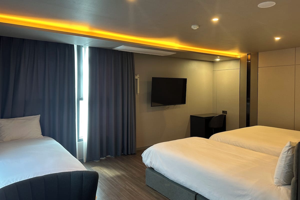 A hotel room with two beds, a flat-screen TV mounted on the wall, and a desk with a chair.