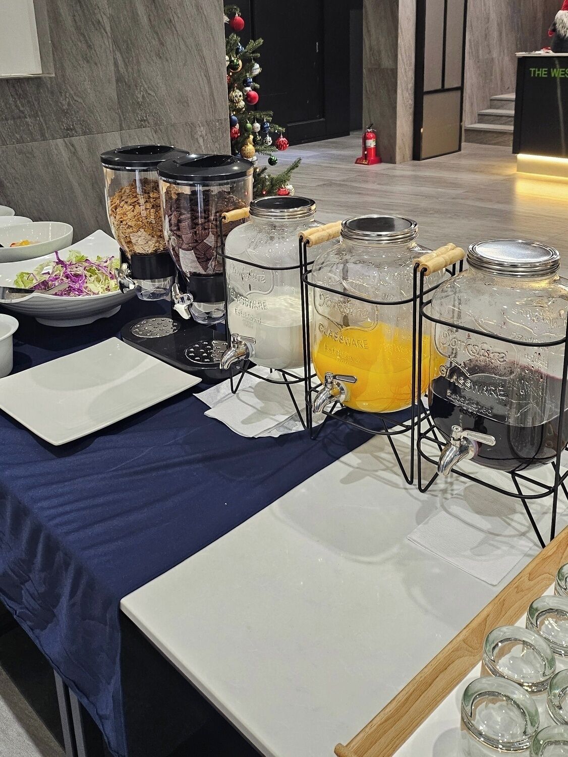 A buffet setup with various food containers and a Christmas tree in the background.