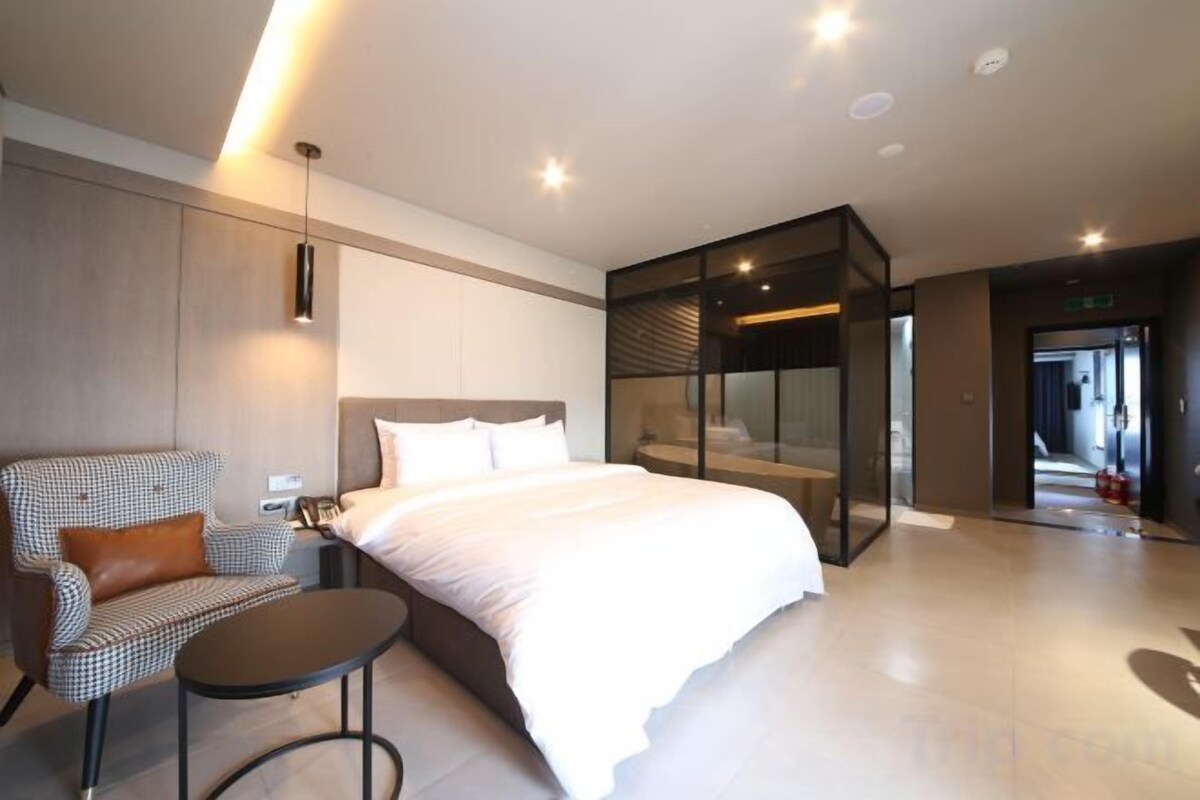 Une chambre d’hôtel moderne dotée d’un grand lit, d’un coin salon et d’une cloison en verre.