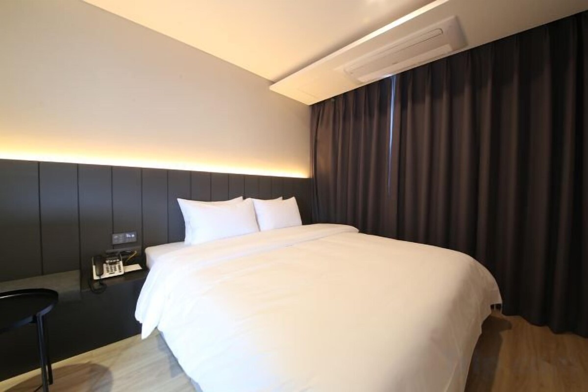 A hotel room with a large bed, a bedside table, and a headboard with built-in lighting.