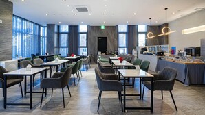 Een moderne eetruimte met meerdere tafels en stoelen, een keukenhoek met een lange aanrecht, en grote ramen voor natuurlijk lichtinval.
