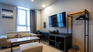 Een moderne woonkamer met een bank, een salontafel, een aan de muur bevestigde televisie en een houten kledingrek.