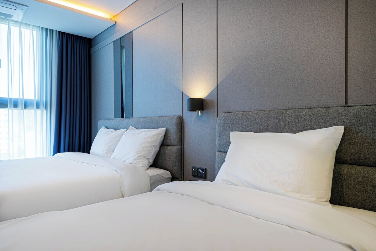 A hotel room with two beds, a wall-mounted light, and a control panel.