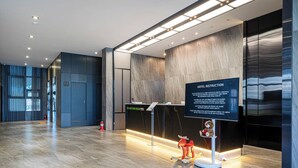 Een moderne hotelontvangsthal met een marmeren vloer, een receptiebalie en een bord met hotelinstructies.