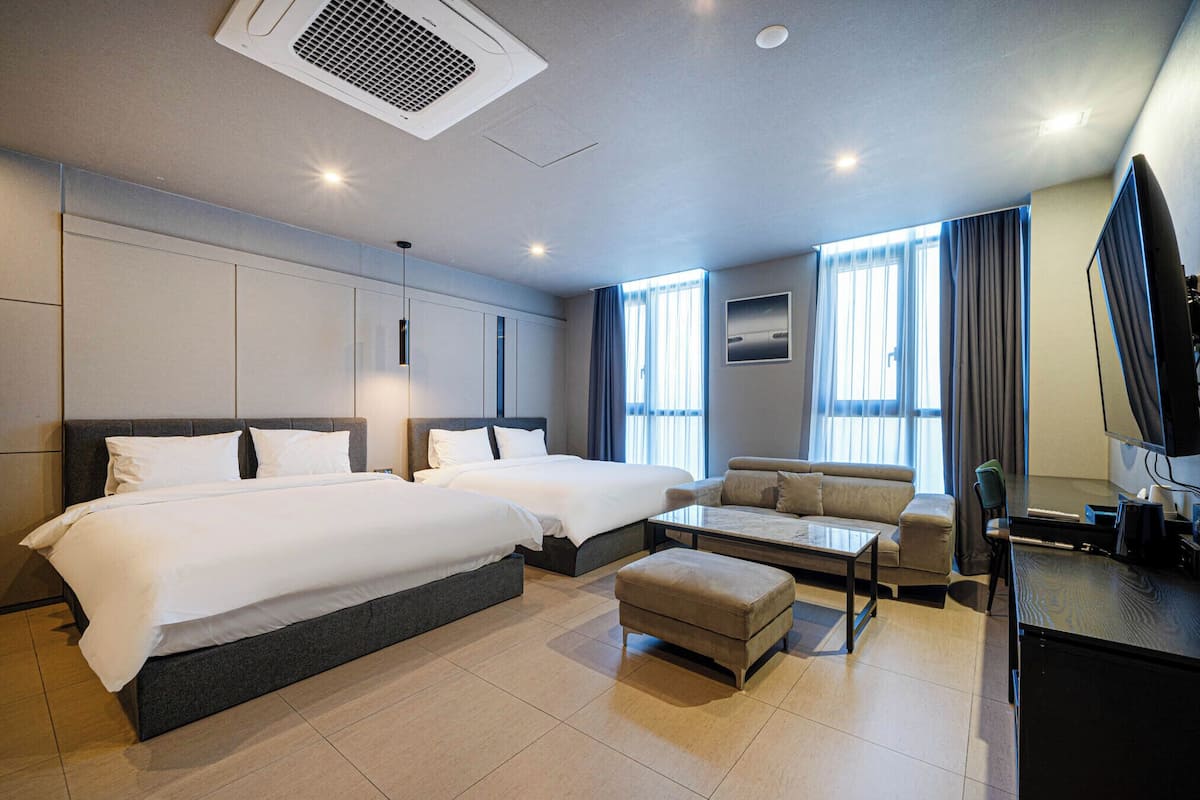 A hotel room with two beds, a sofa, a TV, and a desk.