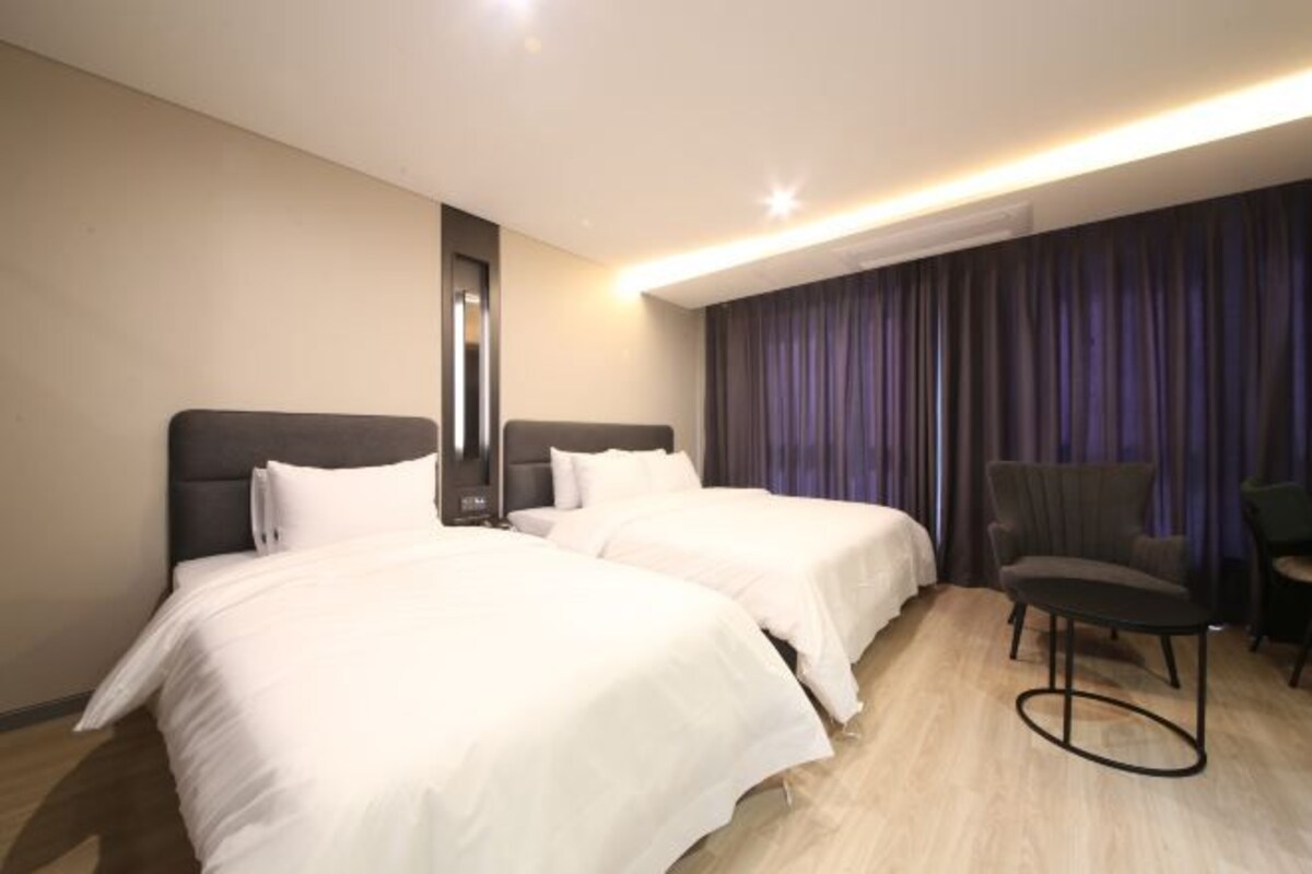 A hotel room with two beds, a chair, and a large window with curtains.