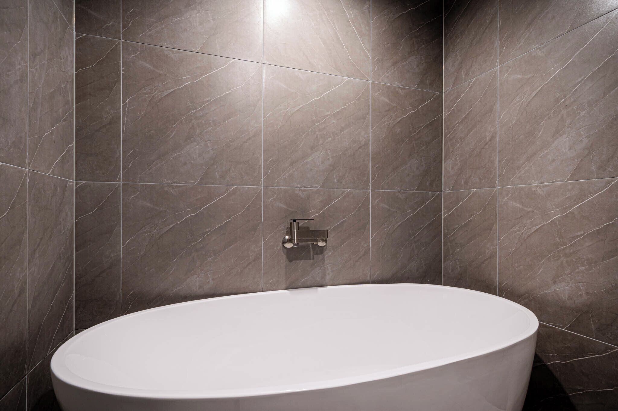 Un baño moderno con una bañera independiente, baldosas de mármol y un grifo de pared.