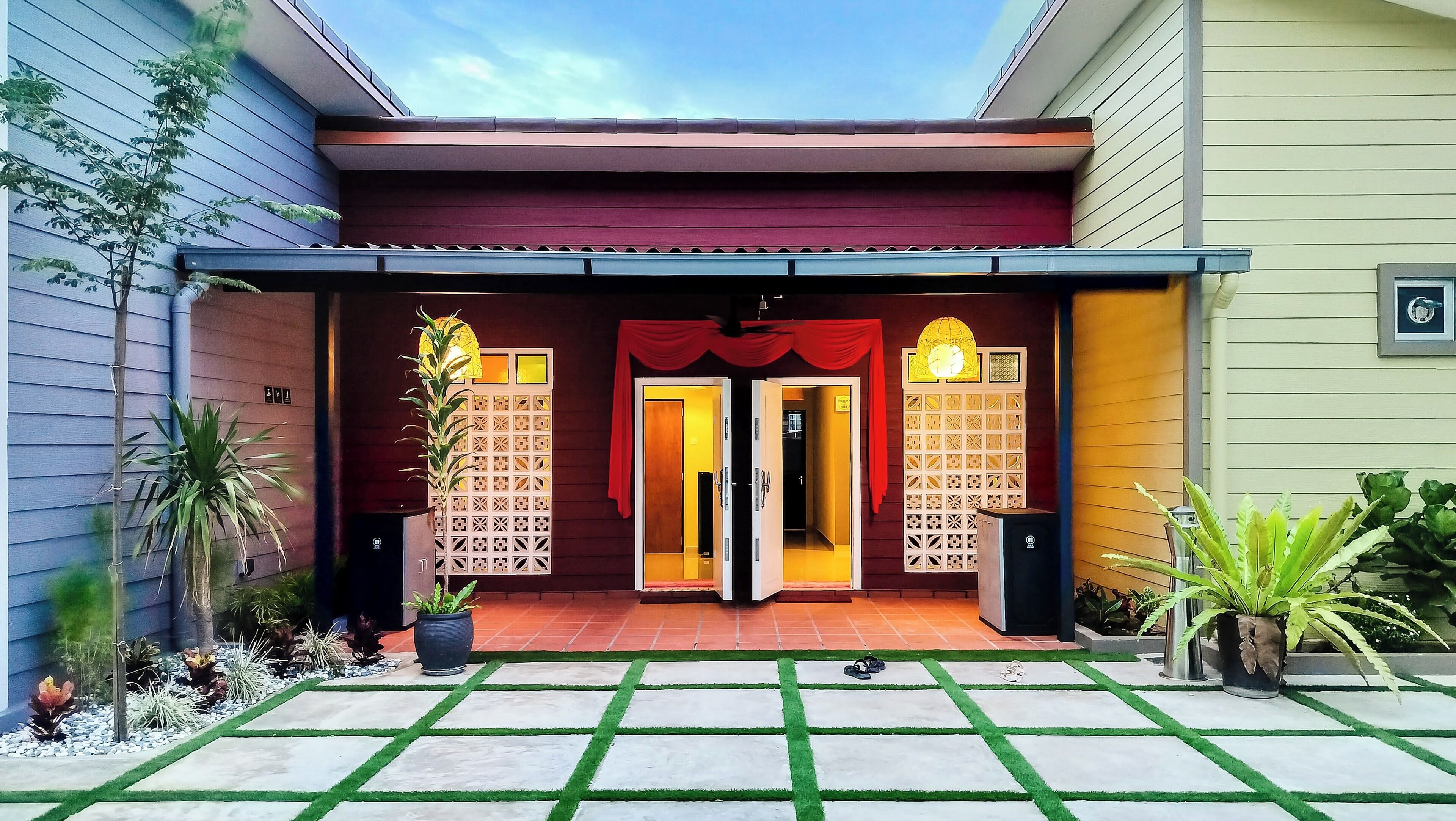 A house entrance with a red awning, two open doors, and a decorative wall with a lattice pattern.