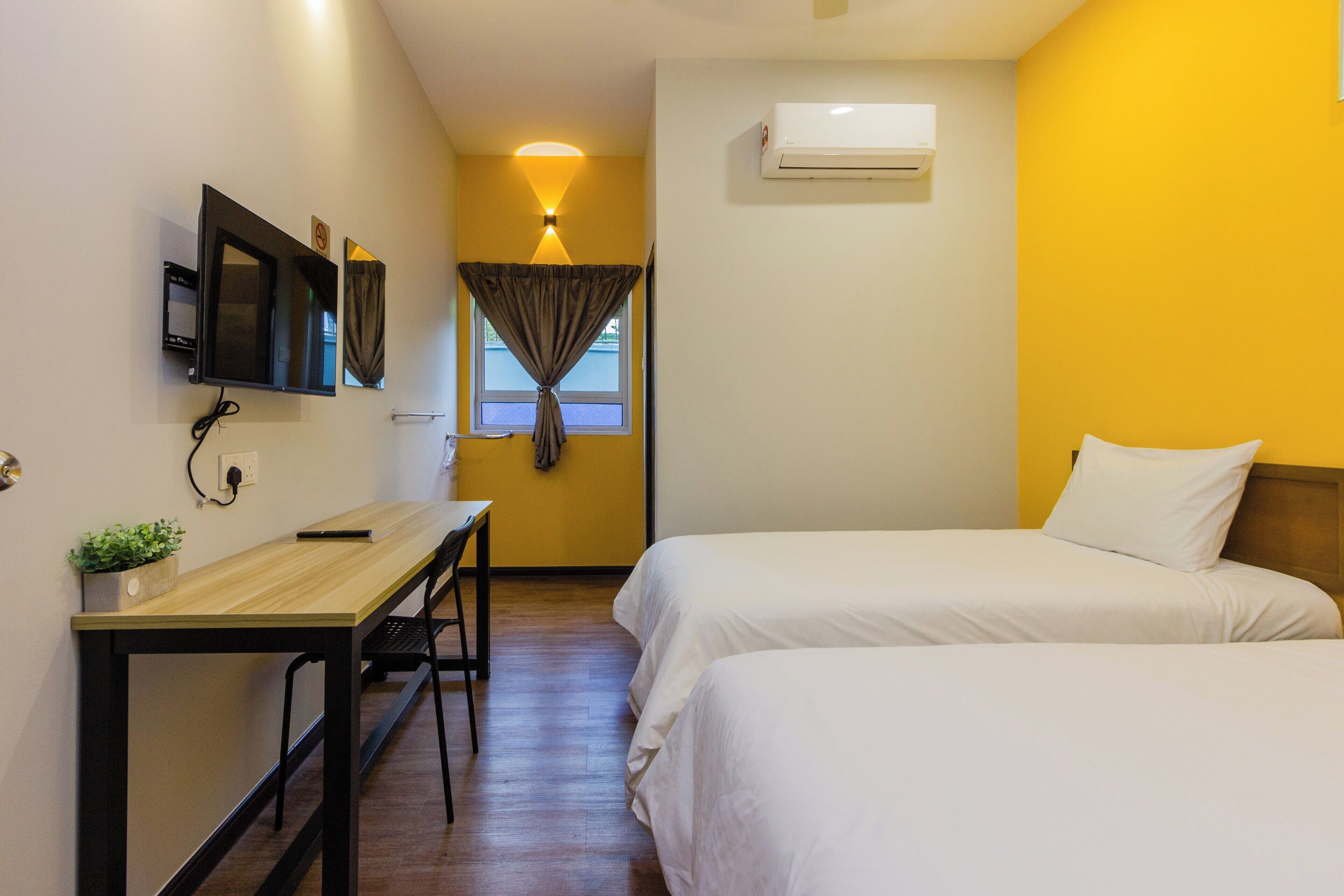 A hotel room with two beds, a desk, a TV, and an air conditioner.