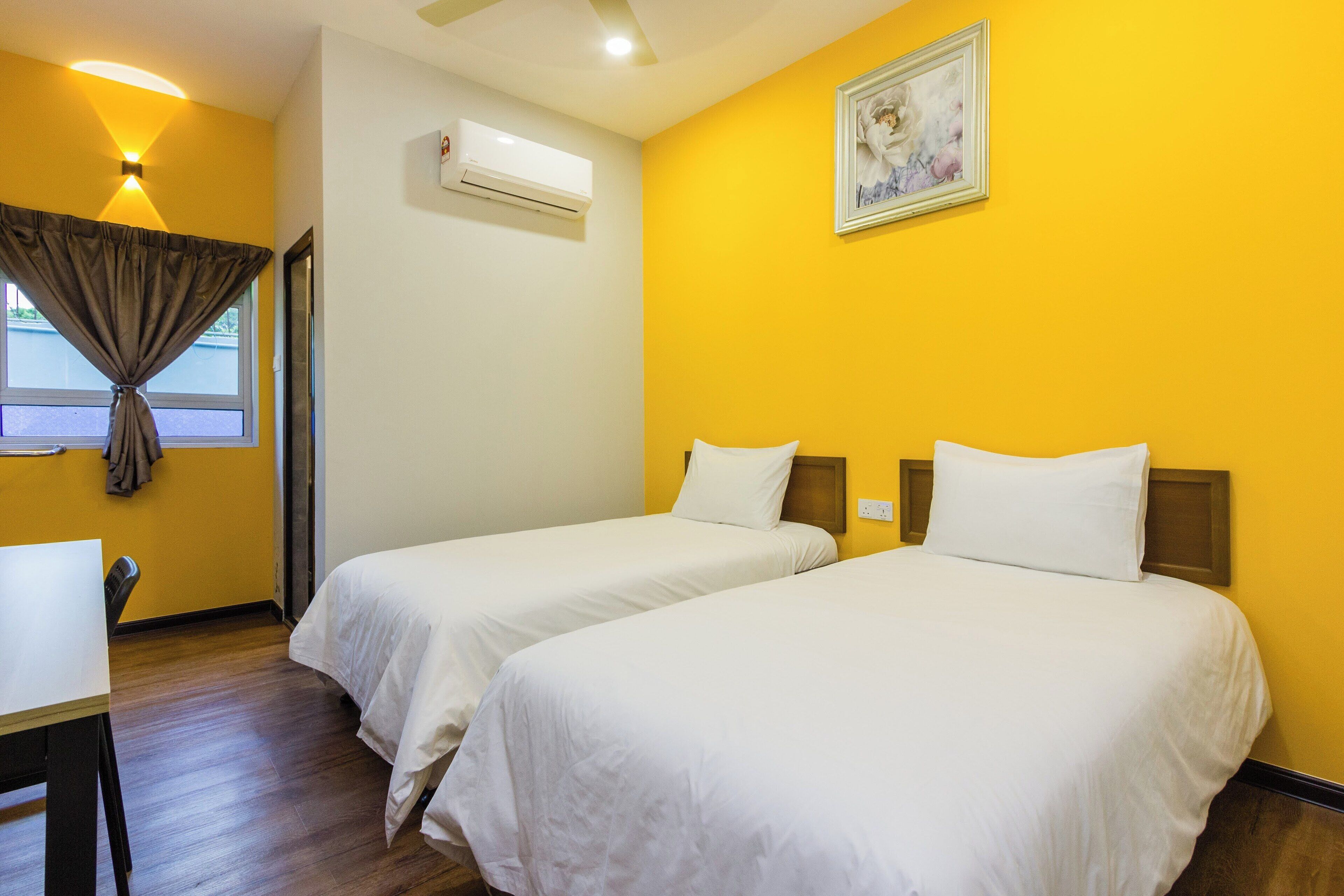 A hotel room with two single beds, a desk, an air conditioning unit, and a window with curtains.