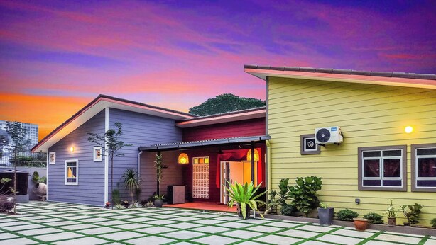 Een tweelaags huis met een betegeld terras, een zichtbare airconditioning en een rode deur.