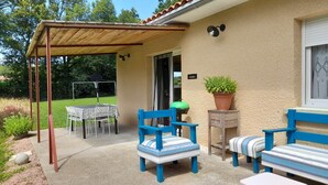 Une terrasse extérieure avec une table et des chaises, un espace salon couvert et un pot de fleurs.