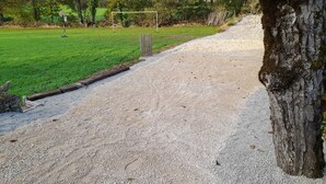 Un chemin de gravier mène à une zone herbeuse où se trouve un poteau de but.