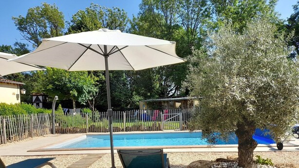 Un espace piscine comprenant une chaise longue, un parasol et un arbre.