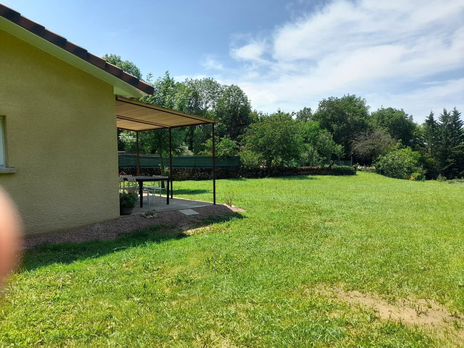 A covered patio area with a table and chairs, a grassy yard, and a stone wall.