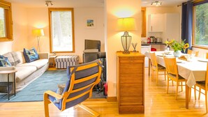 Ein modernes Wohnzimmer mit einer Couch, einem Esstisch für zwei Personen und einer Küche im Hintergrund.