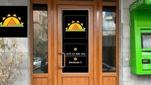 A wooden door with a glass panel, a potted plant, and a green ATM machine to the right. - Areva Hostel (Yerevan)