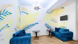 A room with two blue sofas, a small round table, and a wall with a leaf pattern. - Areva Hostel (Yerevan)