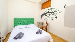 A neatly made bed with a green headboard, a wall mural of a tree with birds, and a small round table with a chair. - Areva Hostel (Yerevan)