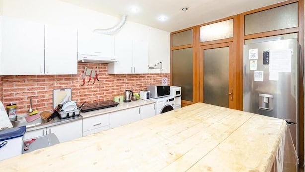 A kitchen with white cabinets, a brick backsplash, a wooden table, and a stainless steel refrigerator. - Areva Hostel (Yerevan)