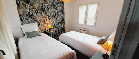 A room with two beds, a patterned wall, a window, and a hanging light fixture.