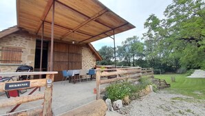 A rustic wooden building with a stone wall, a covered outdoor seating area, and a wooden fence. - Gite HERMINIE et NICOLAS (Cambes)