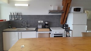 A compact kitchen with a sink, stove, microwave, and a wooden table. - Gite HERMINIE et NICOLAS (Cambes)