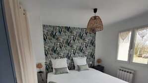 A bedroom with a large bed, a patterned headboard, a bedside lamp, and a window with a view. - Gite HERMINIE et NICOLAS (Cambes)