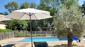 A pool area with a lounge chair, an umbrella, and a tree. - Gite HERMINIE et NICOLAS (Cambes)