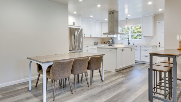 Een moderne keuken met witte kasten, een centraal eiland en een eetgedeelte met vier stoelen.