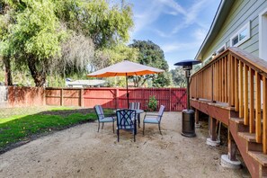 Une terrasse à l’arrière de la maison, avec une table et des chaises, une plateforme en bois et une clôture rouge.