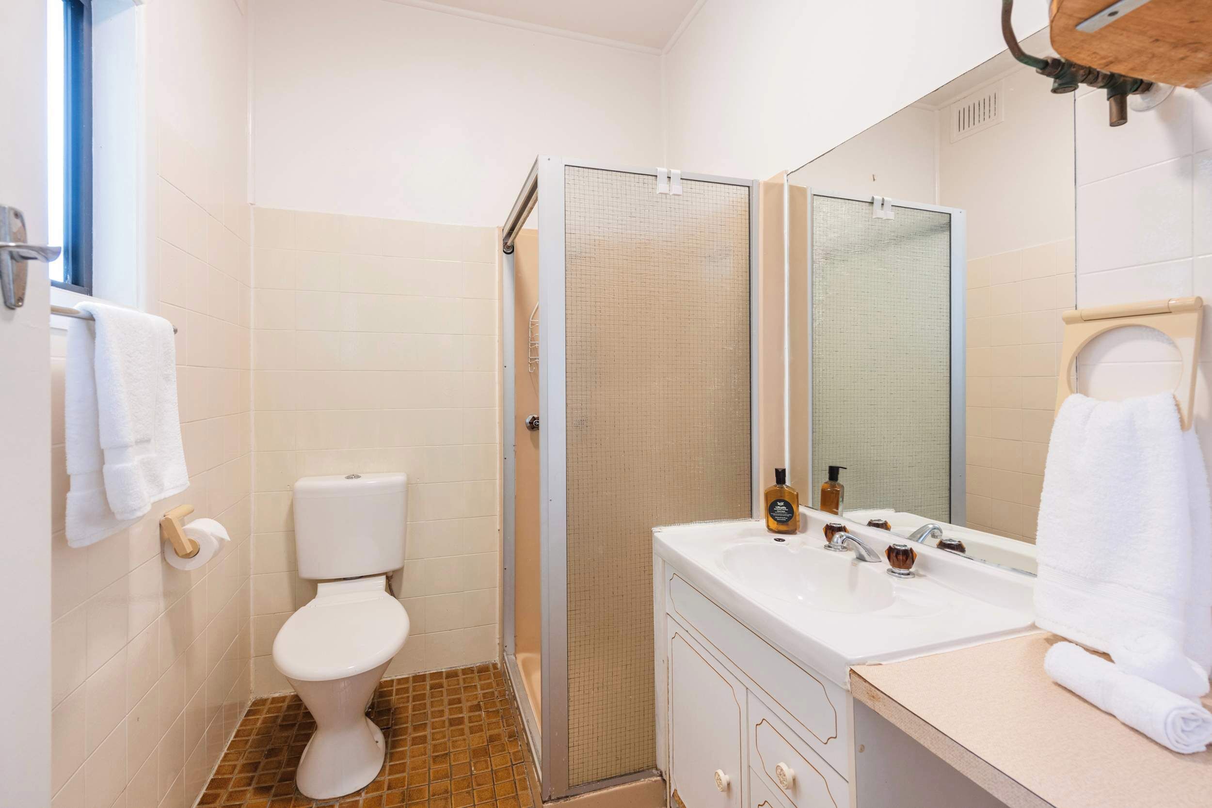 A bathroom with a toilet, shower, sink, and mirror.