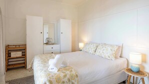 A hotel room with a bed, bedside lamps, a wardrobe, and a small table with a lamp.