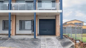 A two-story building with a garage door, a balcony, and a fenced area.