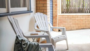 Two white plastic chairs outside a building with a brick wall and a window with blinds.