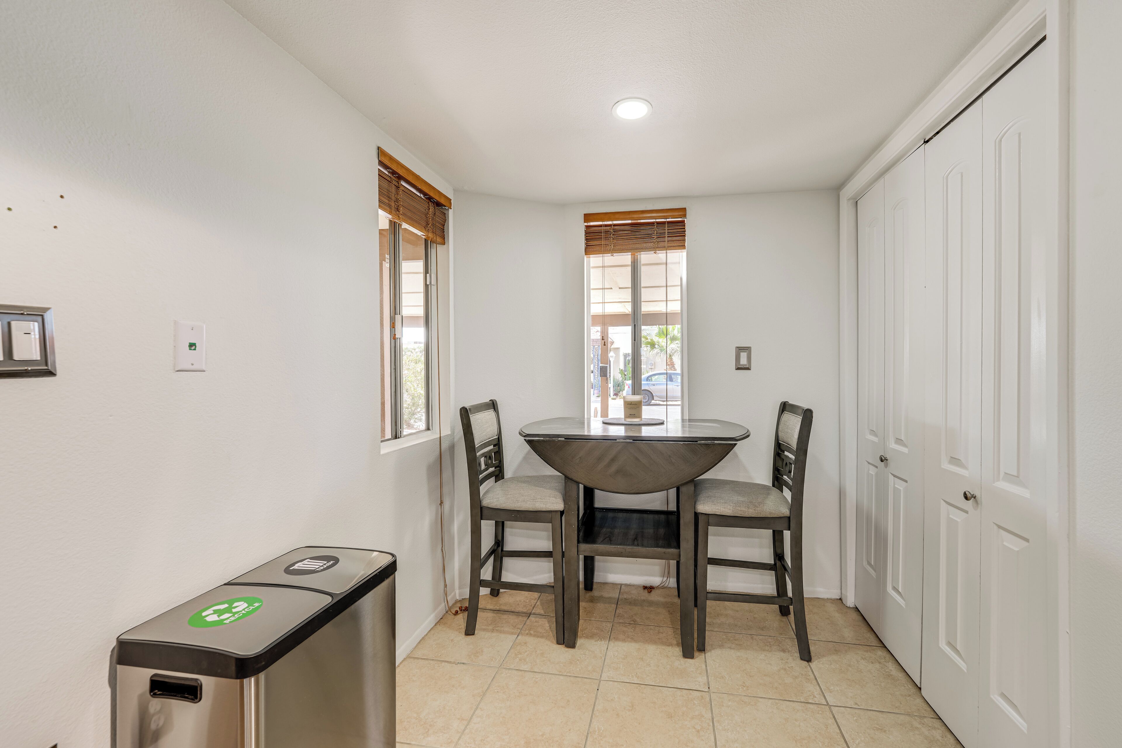 A small dining area with a table and chairs, a trash bin, and a white door.
