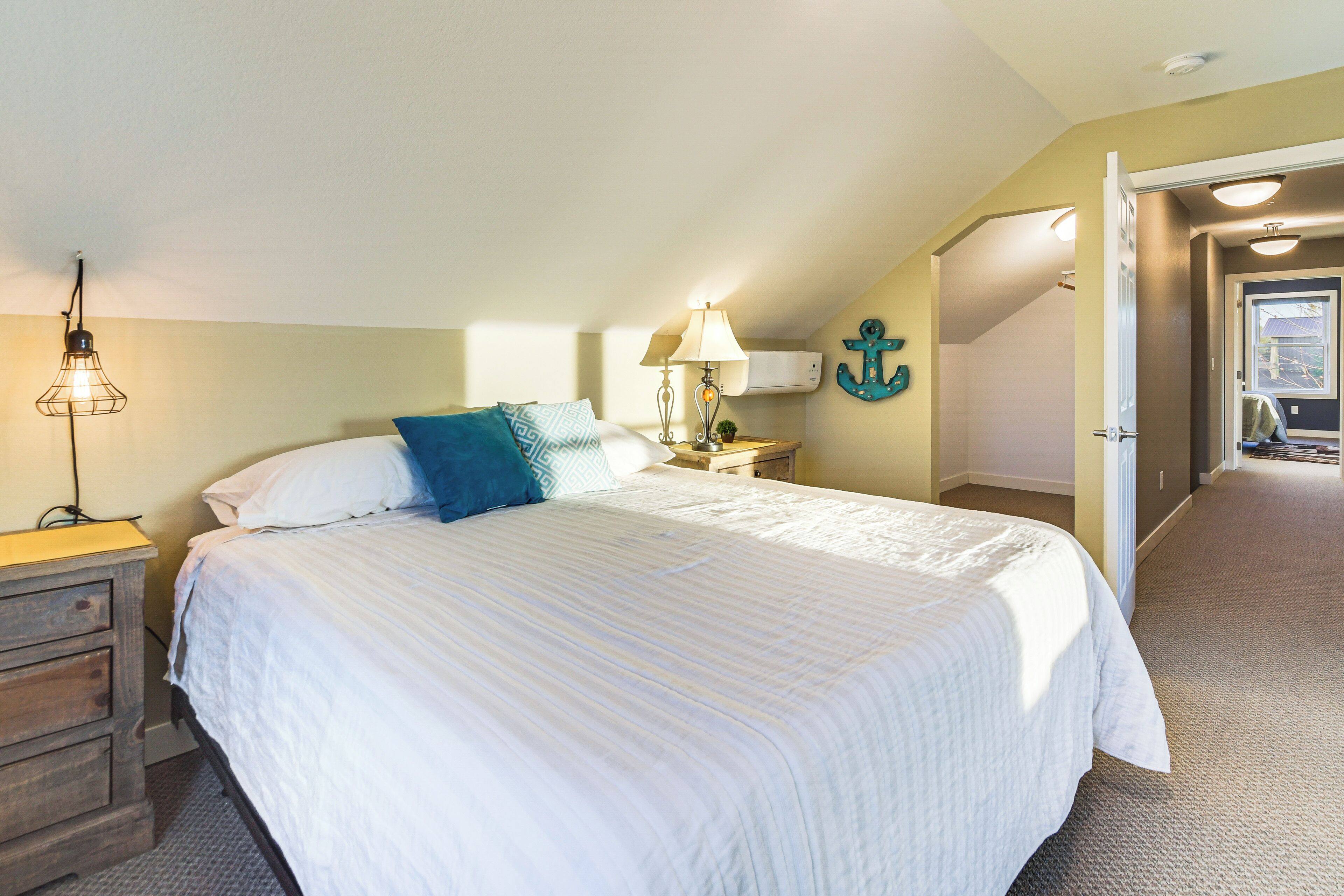 A bedroom with a large bed, a nightstand with a lamp, a dresser, and a wall-mounted anchor decoration.
