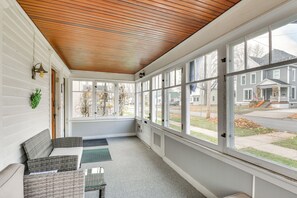 A sunroom with a wooden ceiling, large windows, wicker furniture, and a view of a suburban neighborhood.